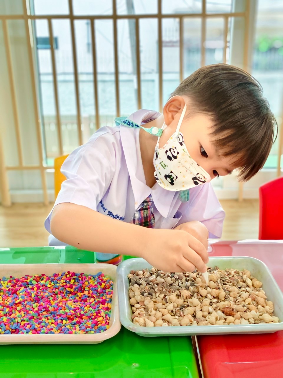 Child exploring texture trays — shells and coloured gravel